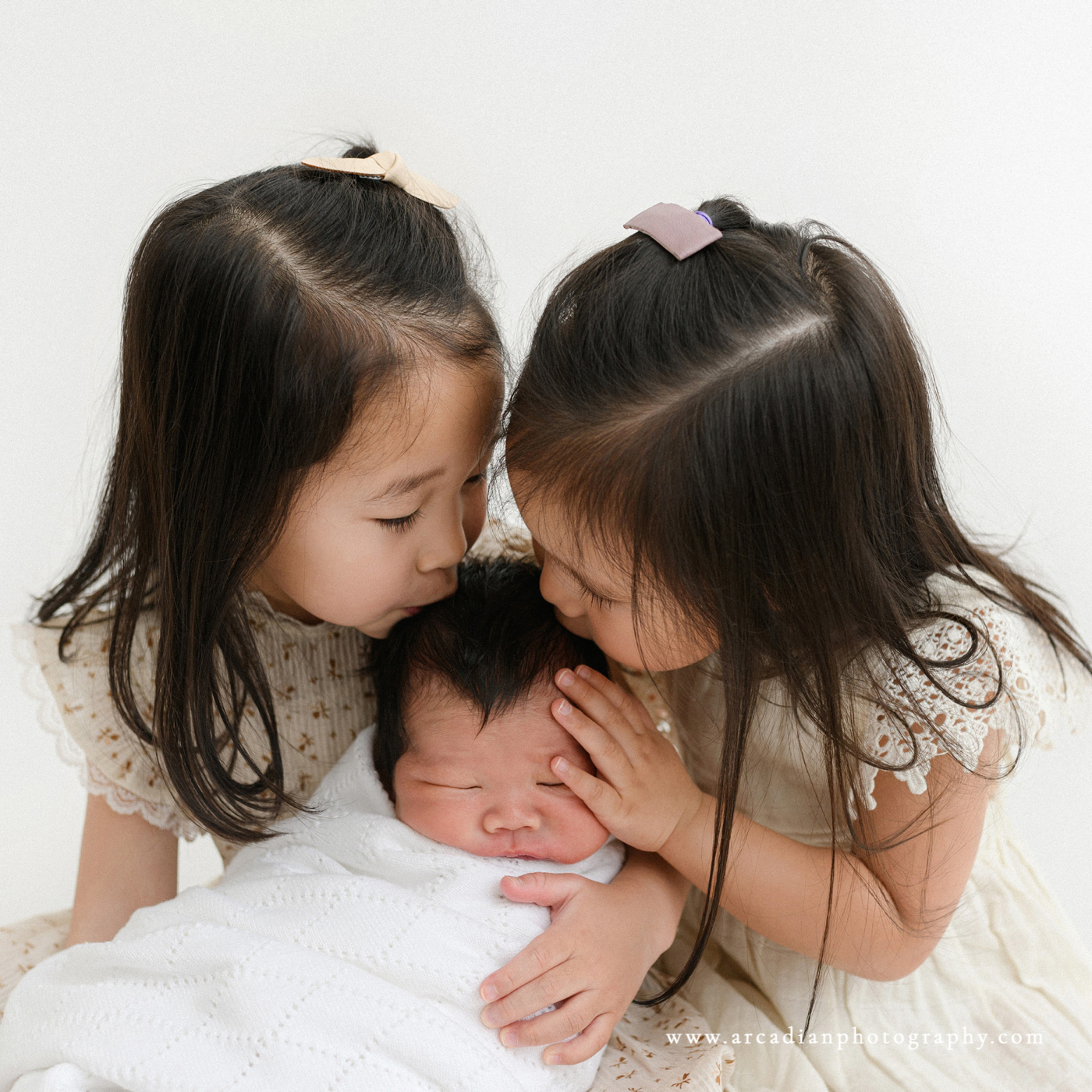 Bib sisters kiss newborn baby brother.
