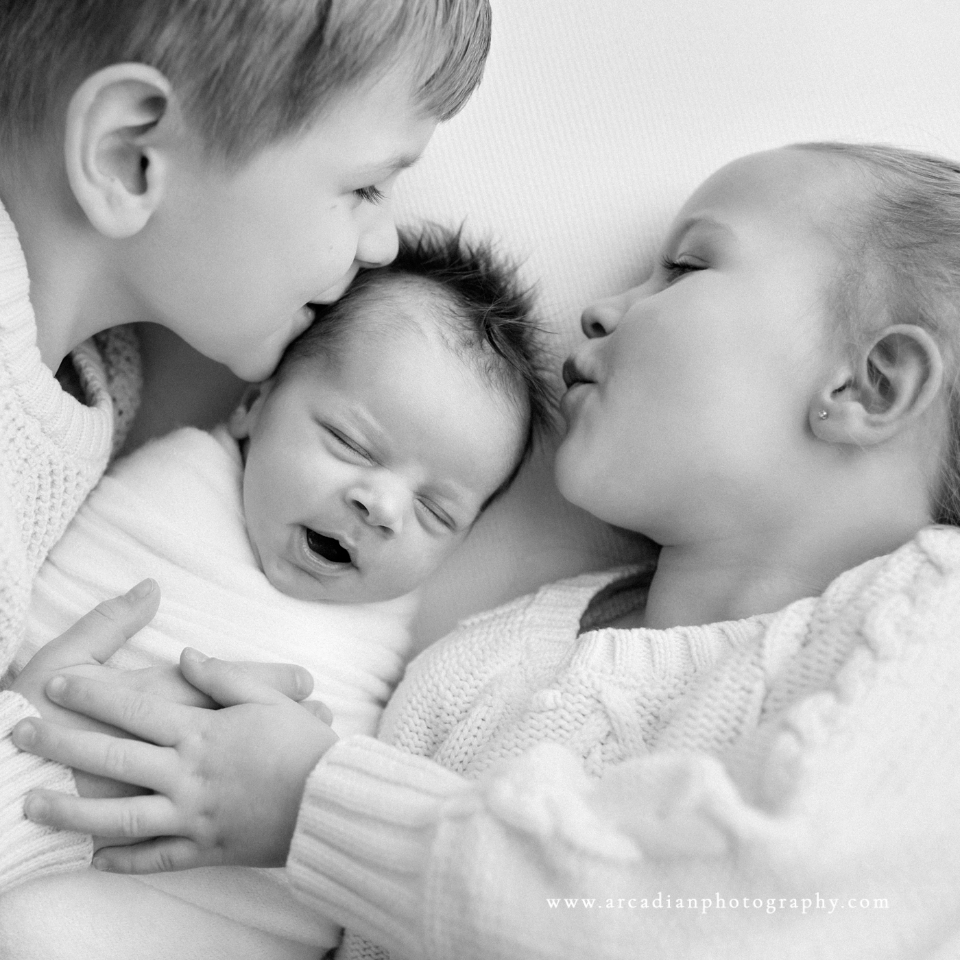 older brother and sister kiss newborn baby brother