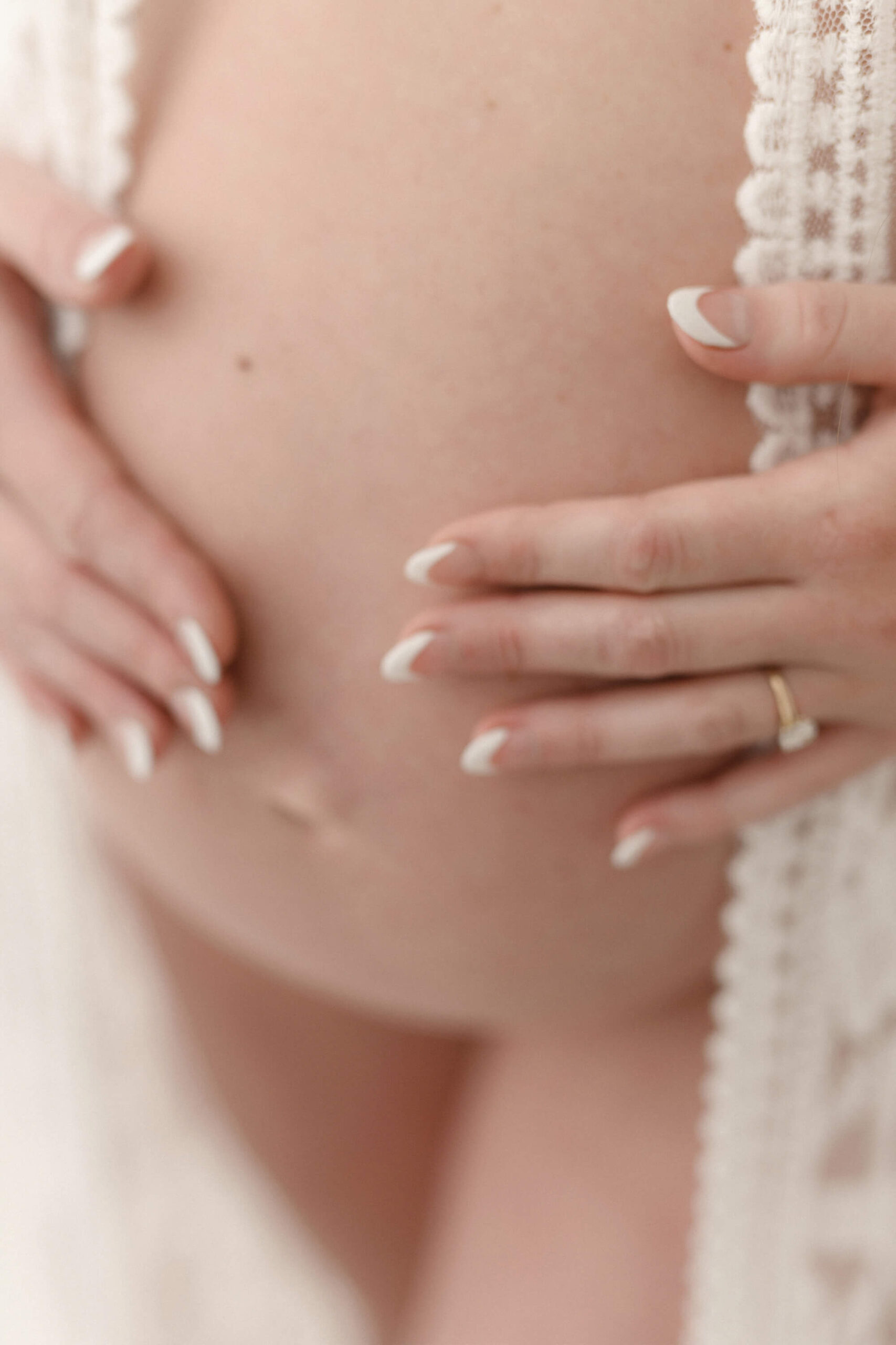 Bare maternity belly detail shot with mother's hands on belly in Portland, Oregon.