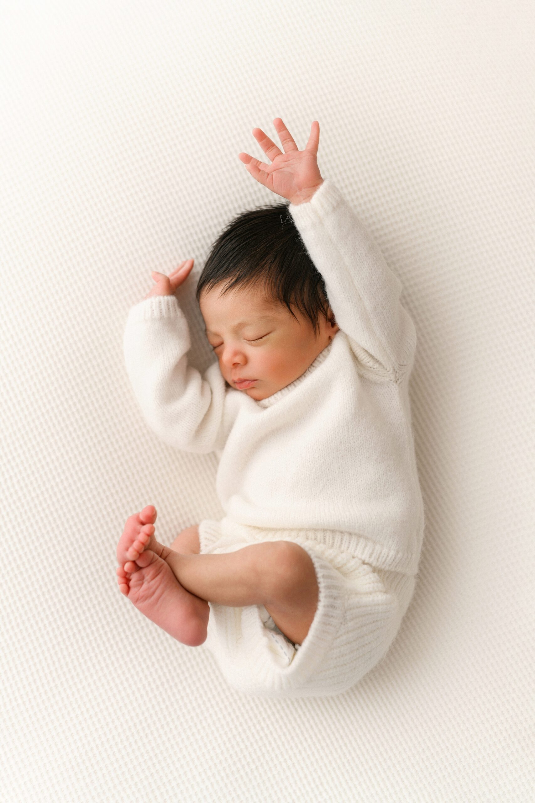 Baby in white outfit, stretching pose.