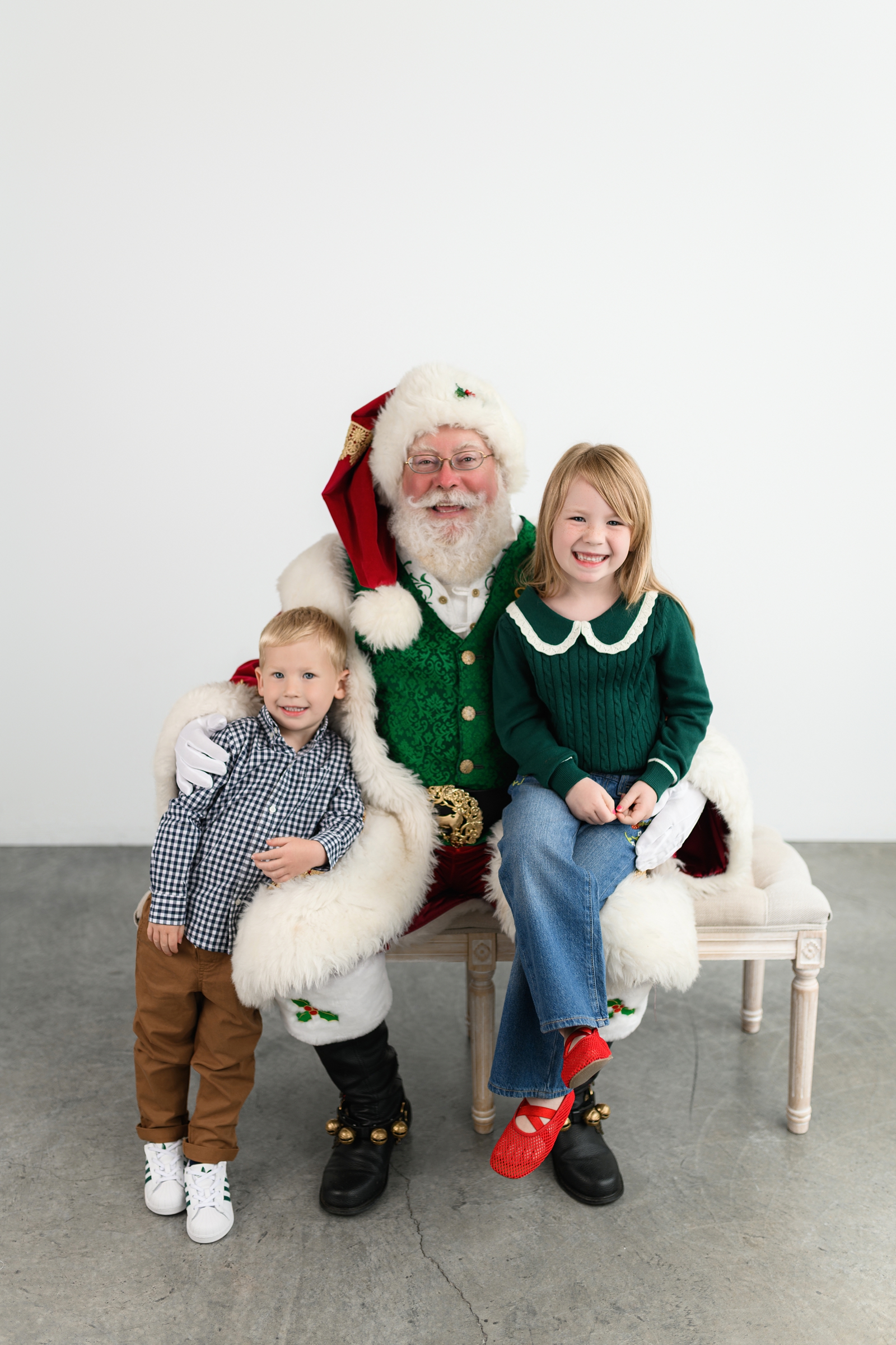 Two smiling children posing with Santa Claus during a Christmas mini session.